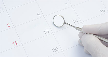 Clinic appointment calendar in the background with a receiptionist's hand holding a dental mirror on a specific date